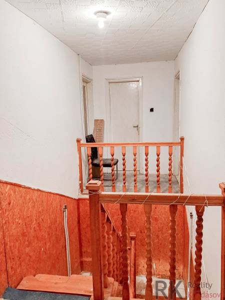 Rodinný dom, Maďarsko, obec Vizsoly - Schodisko s dreveným zábradlím v rodinnom dome, biele steny, osvetlenie so žiarovkou.