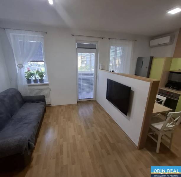 Na prenájom klimatizovaný 2 izbový byt v Moste pri Bratislave - Obývacia izba 2-izbového bytu so sedačkou, televíziou, podlahou s dreveným dekorom a balkónom.