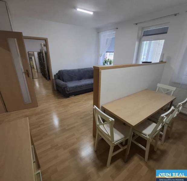 Na prenájom klimatizovaný 2 izbový byt v Moste pri Bratislave - Interiér s pohovkou, jedálenským stolom a podlahou s dreveným dekorom v 2-izbovom byte.