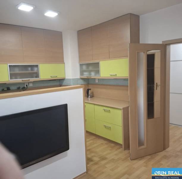 Na prenájom klimatizovaný 2 izbový byt v Moste pri Bratislave - Kuchyňa v 2-izbovom byte s podlahou s dreveným dekorom a farebnými skrinkami.