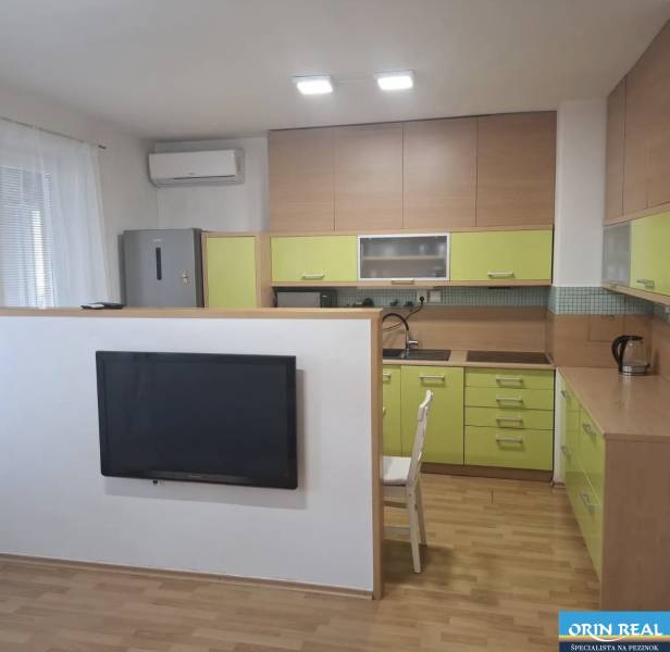 Na prenájom klimatizovaný 2 izbový byt v Moste pri Bratislave - Kuchyňa v 2-izbovom byte s podlahou s dreveným dekorom a zelenými skrinkami.