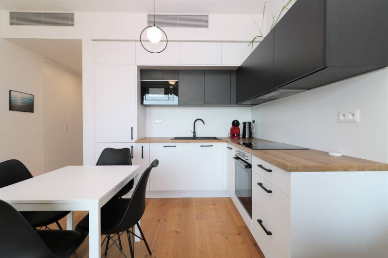 NUERA︱SKY PARK Moderný 2-izbový byt na 6. poschodí, veža 3 - Kuchyňa v 2-izbovom byte s podlahou s dreveným dekorom a čiernymi skrinkami.