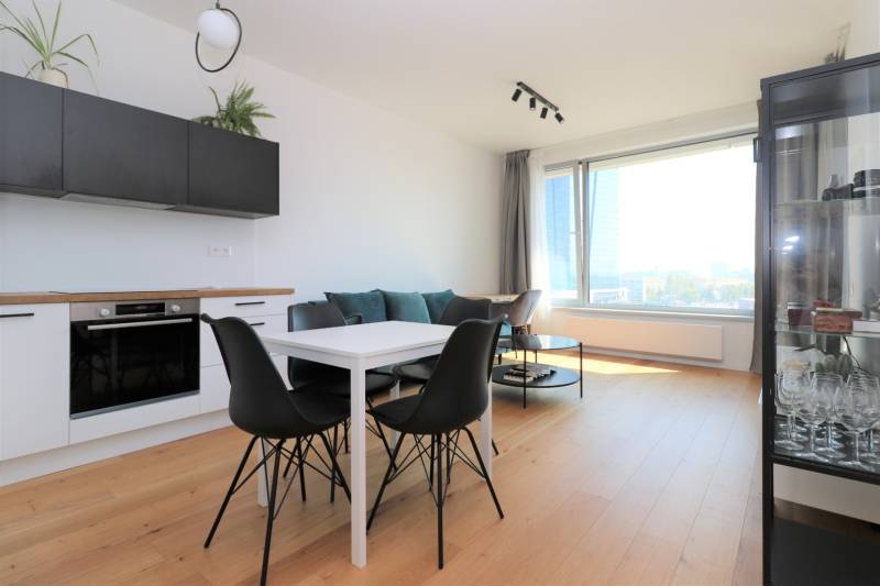 NUERA︱SKY PARK Moderný 2-izbový byt na 6. poschodí, veža 3 - Kuchyňa a jedálenský stôl s čiernymi stoličkami v 2-izbovom byte s podlahou s dreveným dekorom.