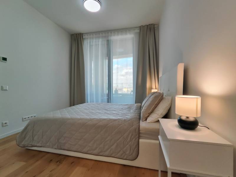 NUERA︱SKY PARK Moderný 2-izbový byt na 6. poschodí, veža 3 - Spálňa v 2-izbovom byte s posteľou, nočným stolíkom a podlahou s dreveným dekorom.