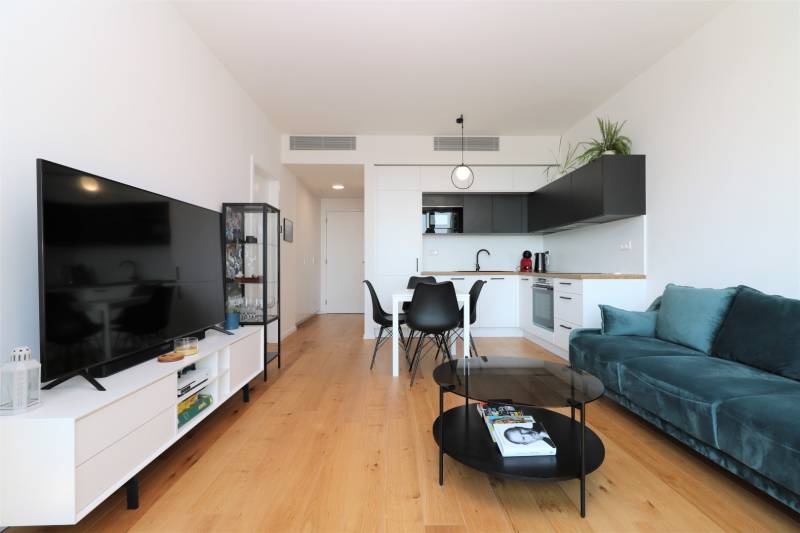 NUERA︱SKY PARK Moderný 2-izbový byt na 6. poschodí, veža 3 - Obývacia izba s kuchyňou v 2-izbovom byte, podlaha s dreveným dekorom, TV a sedacia súprava.