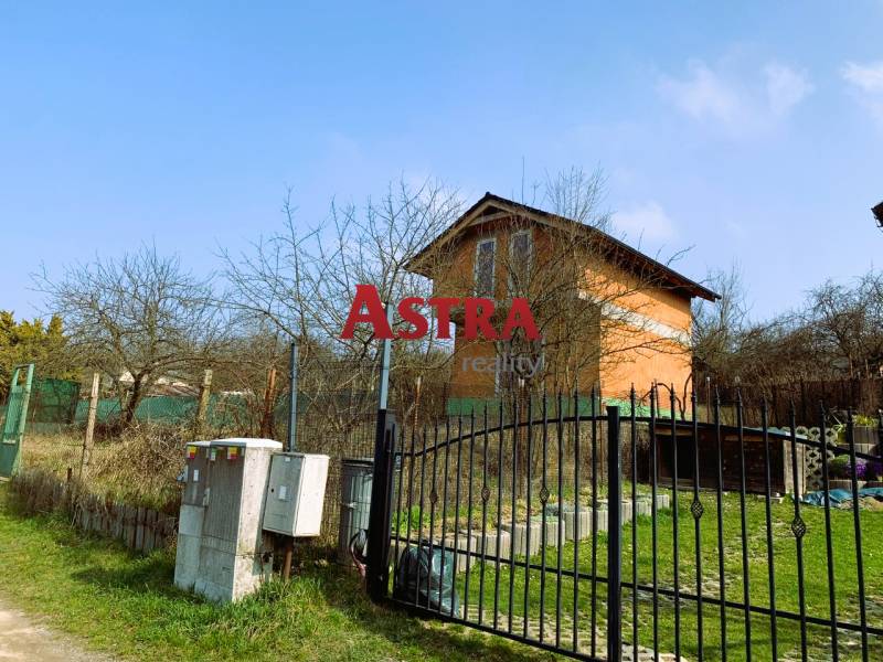 CHATA UZAVRETÁ HRUBÁ STAVBA, KOŠICKÁ NOVÁ VES - GEDER - Na obrázku je chata obklopená stromami a plotom na trávnatom pozemku.