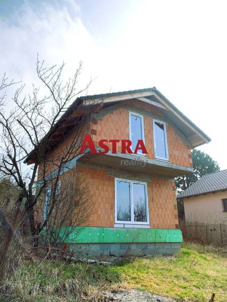 CHATA UZAVRETÁ HRUBÁ STAVBA, KOŠICKÁ NOVÁ VES - GEDER - Dvojpodlažná chata v rozostavanom stave, obklopená stromami a trávou na vidieckom pozemku.