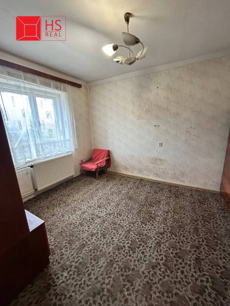Predaj staršieho RD vo Dvoroch nad Žitavou - Izba v rodinnom dome s kobercovou podlahou, jednoduchým kreslom a závesmi.