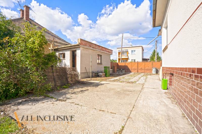 REZERVOVANÉ 3-IZBOVÝ RD NA PRIESTRANNOM POZEMKU, VRAKÚ - Dvor rodinného domu vo Vrakúni s prízemnou prístavbou a oplotením na slnečný deň.