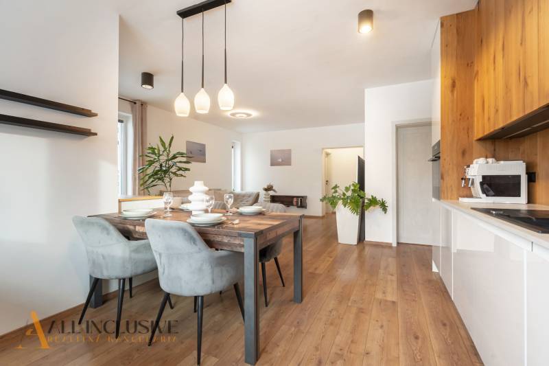 Rezervované 3-izbový byt so záhradou, Šamorín - Jedálenská a kuchynská časť 3-izbového bytu s podlahou s dreveným dekorom a závesným osvetlením.