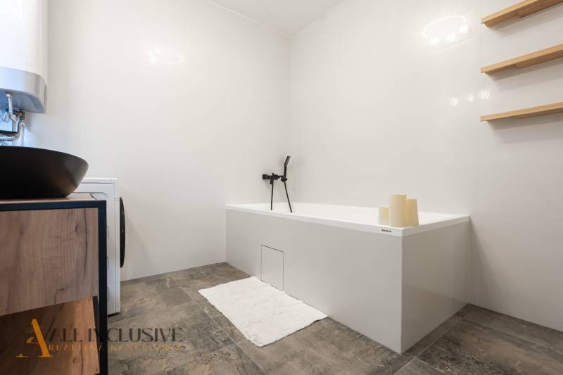 Rezervované 3-izbový byt so záhradou, Šamorín - Kúpeľňa v 3-izbovom byte s bielou vaňou, umývadlom a policami na stene.