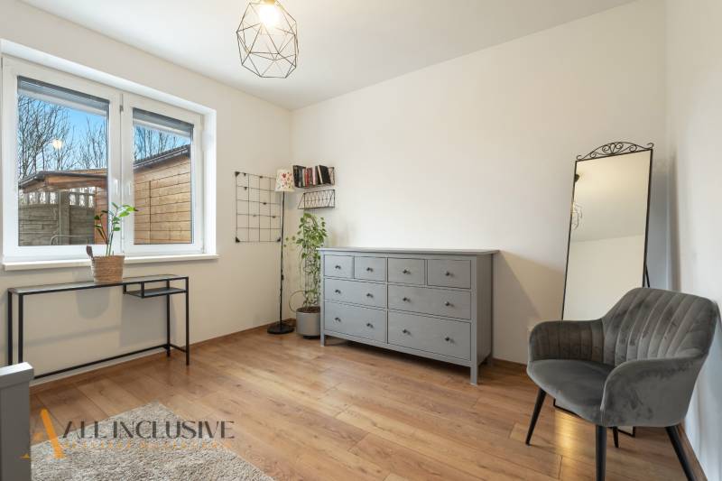 Rezervované 3-izbový byt so záhradou, Šamorín - Interiér 3-izbového bytu s podlahou s dreveným dekorom, sivou komodou a čalúneným kreslom.