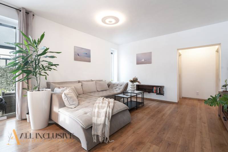 Rezervované 3-izbový byt so záhradou, Šamorín - Obývačka v 3-izbovom byte s podlahou s dreveným dekorom a pohodlnou sedačkou.