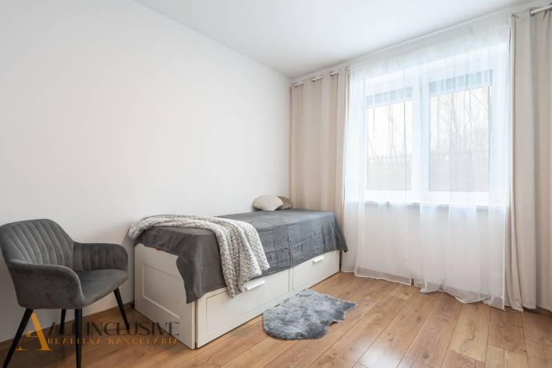 Rezervované 3-izbový byt so záhradou, Šamorín - Svetlá izba v 3-izbovom byte s posteľou, kreslom a podlahou s dreveným dekorom.