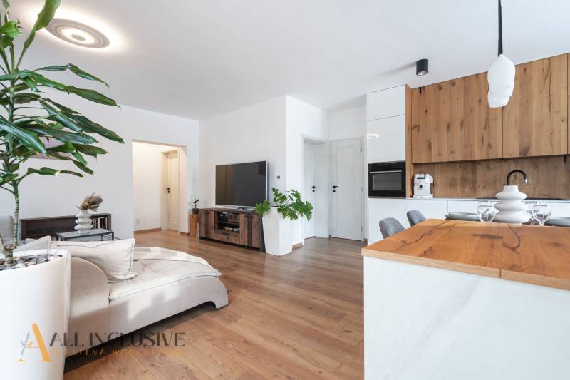 Rezervované 3-izbový byt so záhradou, Šamorín - Obývacia izba so sedačkou, dreveným dekorom a rastlinami v 3-izbovom byte.