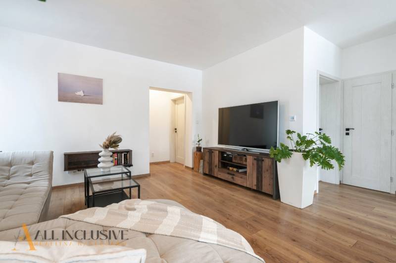 Rezervované 3-izbový byt so záhradou, Šamorín - Interiér 3-izbového bytu s podlahou s dreveným dekorom, pohovkou, TV a rastlinou.