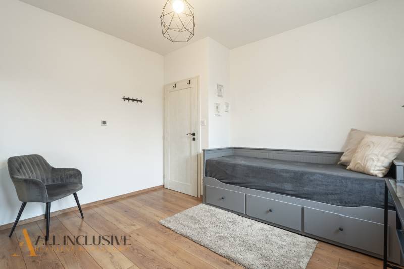 Rezervované 3-izbový byt so záhradou, Šamorín - Izba v 3-izbovom byte s posteľou, šedým kreslom a podlahou s dreveným dekorom.