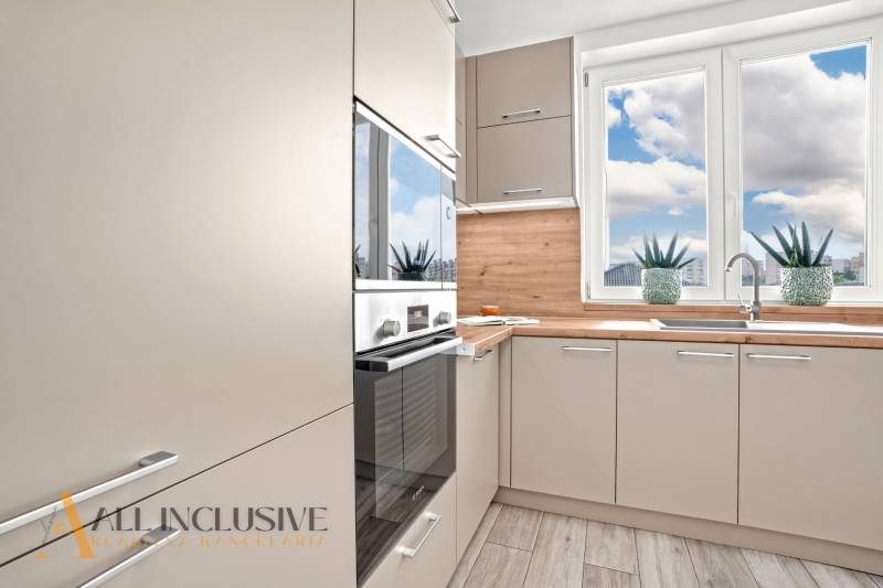 NA PRENÁJOM 3-IZB BYT S BALKÓNOM A ZÁHRADOU,DUN.STREDA - Svetlá kuchyňa s podlahou s dreveným dekorom v 3-izbovom byte, veľké okná a rastliny.