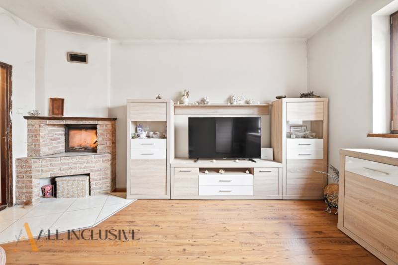 Na predaj 3-izbový rodinný dom, Topoľníky - Obývacia izba v rodinnom dome s krbom, televíziou a podlahou s dreveným dekorom.