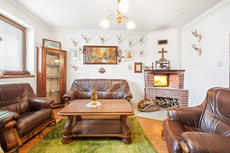 Na predaj 3-izbový rodinný dom, Topoľníky - Obývačka v rodinnom dome s krbom, koženými sedačkami a loveckými trofejami na stene.