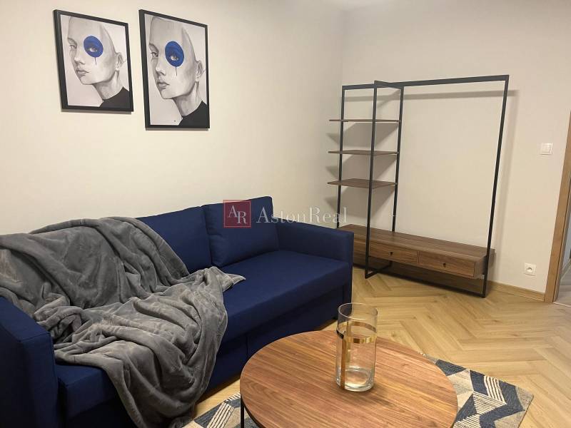 EXKLUZÍVNE-PREDAJ 3-IZBOVÝ BYT POPRAD, širšie centrum 80 m2 s gar.st. - Obývacia izba s modrou sedačkou, modernými obrazmi a policovým systémom v 3-izbovom byte.