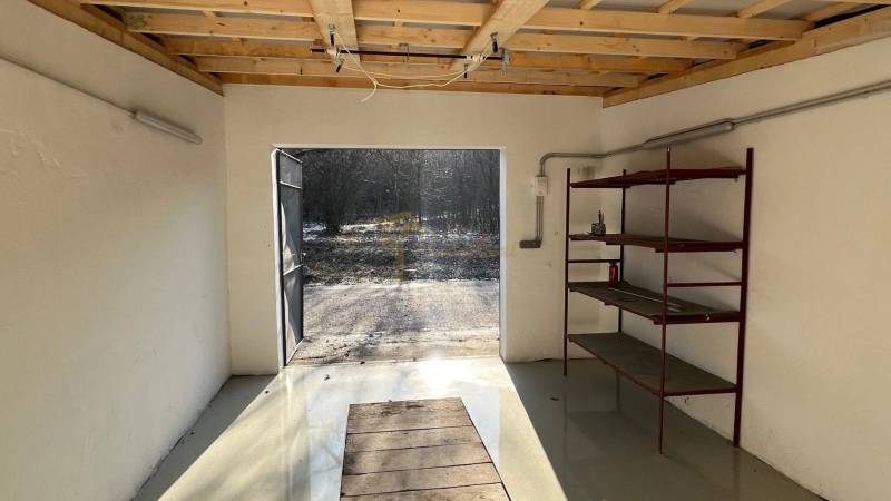 Zrekonštruovaná veľká garáž na ul. Agátova, Dúbravka s pozemkom - Garáže na Agátovej ulici v Bratislave-Dúbravke so železnými policami a otvorenými dverami.