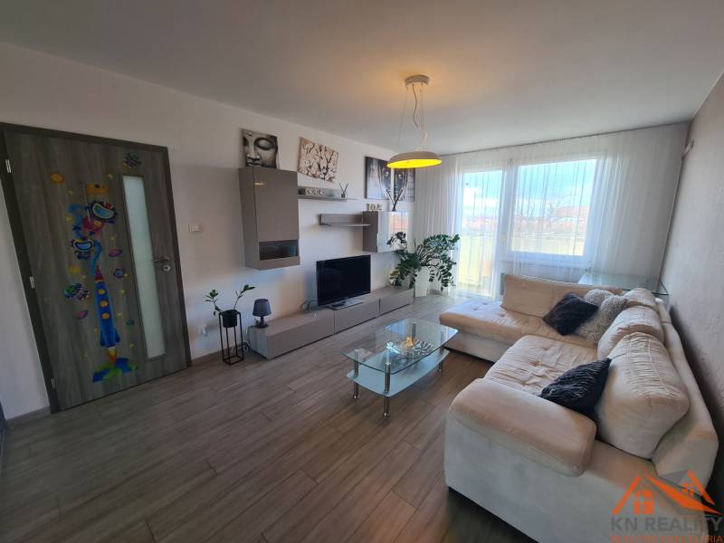 Reprezentatívny 2 izb.byt na prenájom SOHO TOWER Komárno ! - Obývacia izba v 2-izbovom byte s podlahou s dreveným dekorom a priestrannou pohovkou.