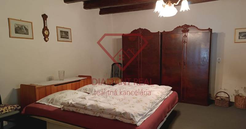 Na predaj RD na bývanie alebo investičná príležitosť Horné Saliby - Spálňa v rodinnom dome s dreveným stropom, starožitnou skriňou a klasickým lustrom.