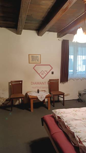 Na predaj RD na bývanie alebo investičná príležitosť Horné Saliby - Izba v rodinnom dome s dreveným stropom, dvomi stoličkami a stolíkom.