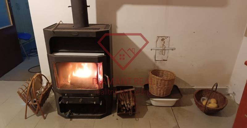 Na predaj RD na bývanie alebo investičná príležitosť Horné Saliby - Krbová pec v rodinnom dome, vedľa ktorej sú košíky s drevom a ovocím.