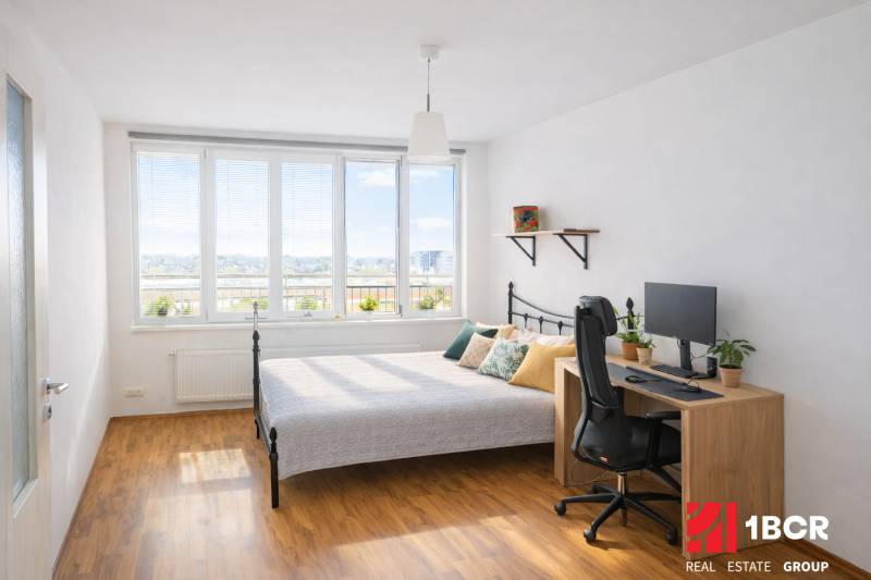 INVESTIČNÉ BÝVANIE V TOP LOKALITE: 2-IZBOVÝ BYT, JÉGÉHO UL, BRATISLAVA - Spálňa v 2-izbovom byte s posteľou, stolom, počítačom a podlahou s dreveným dekorom.