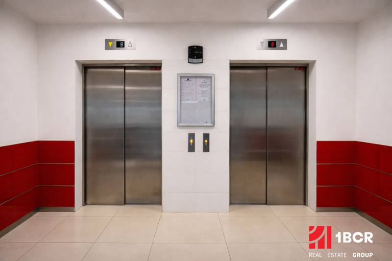 INVESTIČNÉ BÝVANIE V TOP LOKALITE: 2-IZBOVÝ BYT, JÉGÉHO UL, BRATISLAVA - Dva výťahy so sivými dverami a bielymi stenami s červenými obkladmi.