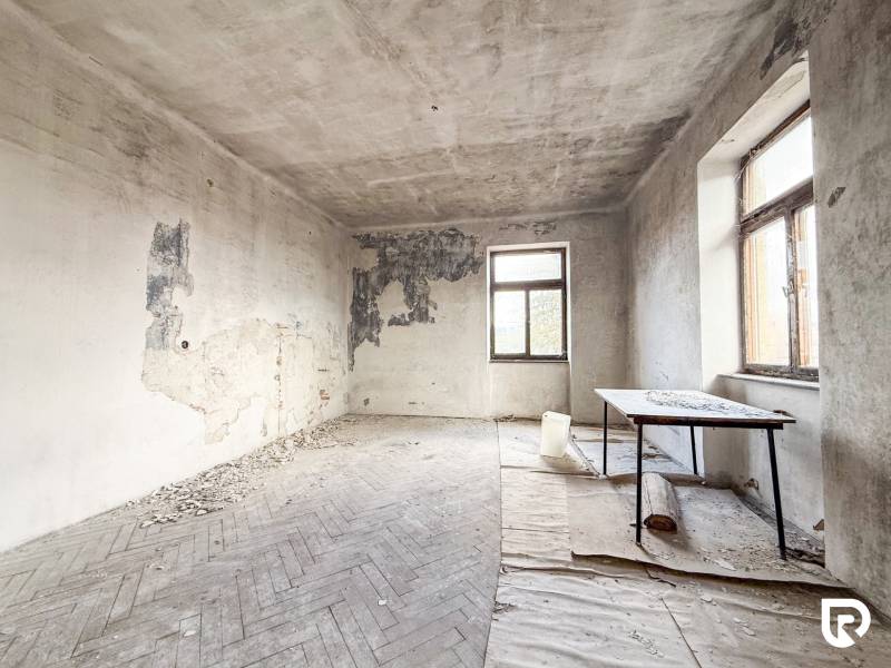 Rodinný dom (bytovka) s pozemkom 554m2, Bobotská Lehota - Opustená miestnosť s poškodenými stenami a podlahou s dreveným dekorom v rodinnom dome.