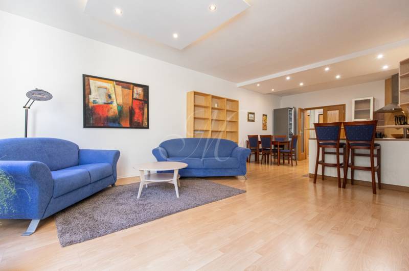 Priestranný 3-izbový byt s loggiou, Staré Mesto - Obývacia izba s modrými sedačkami, farebným obrazom a podlahou s dreveným dekorom v 3-izbovom byte.