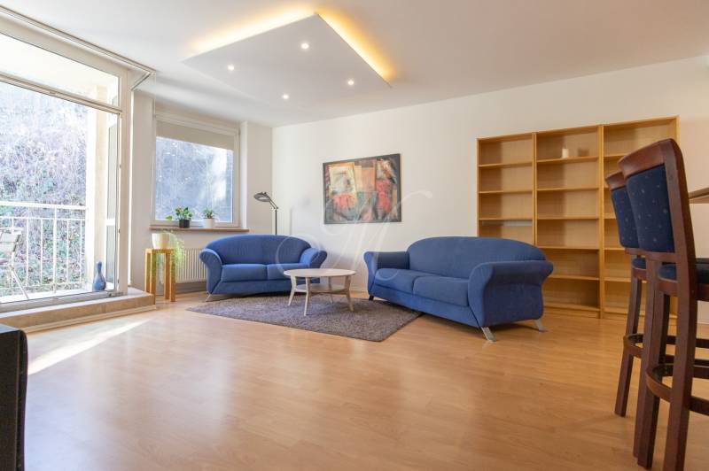 Priestranný 3-izbový byt s loggiou, Staré Mesto - Obývacia izba v 3-izbovom byte s modrými sedačkami a podlahou s dreveným dekorom.