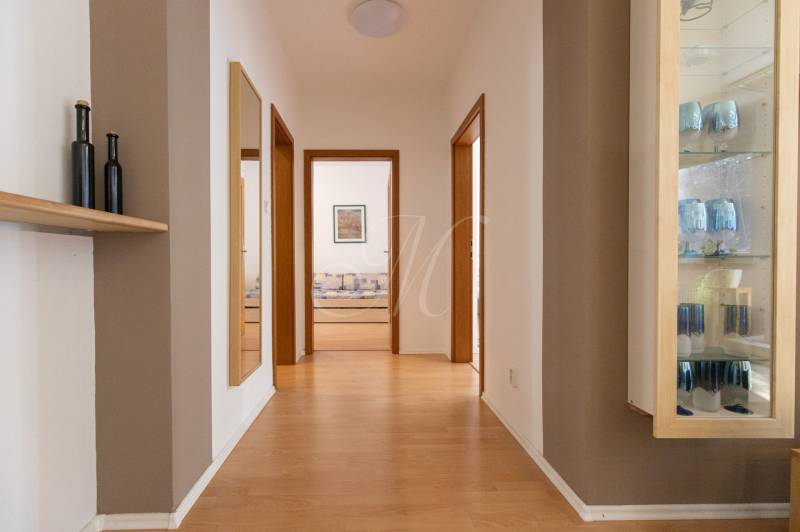 Priestranný 3-izbový byt s loggiou, Staré Mesto - Chodba v 3-izbovom byte s podlahou s dreveným dekorom, zrkadlom a sklenenou vitrínou.