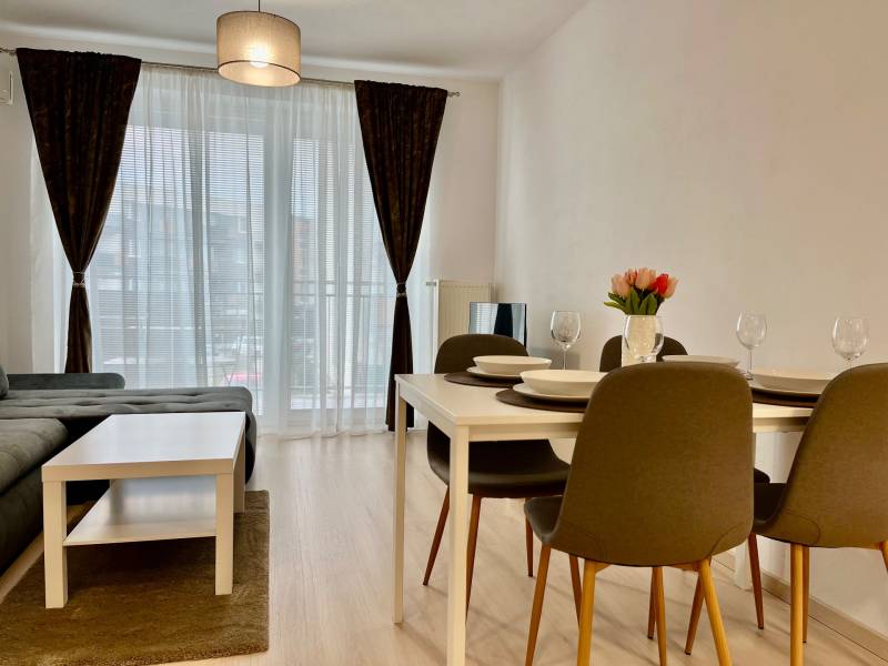 PRENÁJOM NOVOSTAVBA 2 izb.byt, BALKÓN, PARKOVACIE MIESTO, BIELY KOSTOL - 2-izbový byt s podlahou s dreveným dekorom, jedálenským stolom a pohovkou.