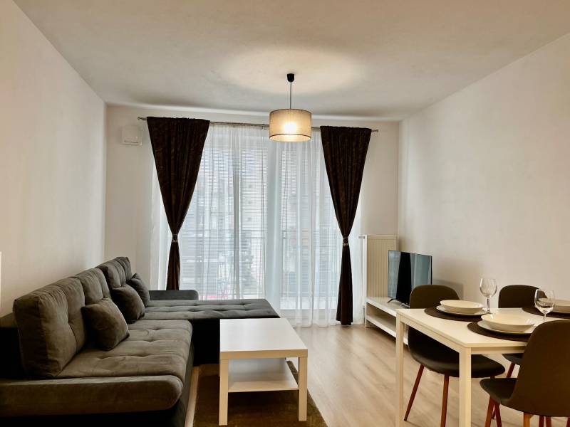 PRENÁJOM NOVOSTAVBA 2 izb.byt, BALKÓN, PARKOVACIE MIESTO, BIELY KOSTOL - Obývacia izba v 2-izbovom byte s pohovkou, jedálenským stolom a podlahou s dreveným dekorom.