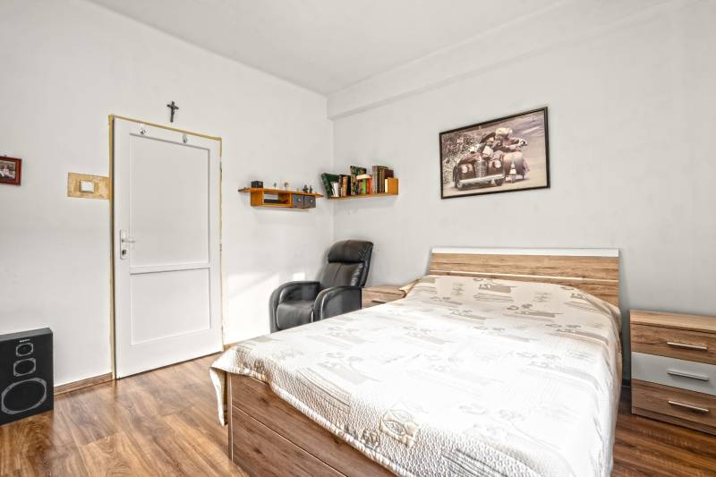 NA PREDAJ VÝNIMOČNÝ RODINNÝ DOM VO VEĽKOM MEDERI - Izba v rodinnom dome s posteľou, kreslom a policou, podlaha s dreveným dekorom.