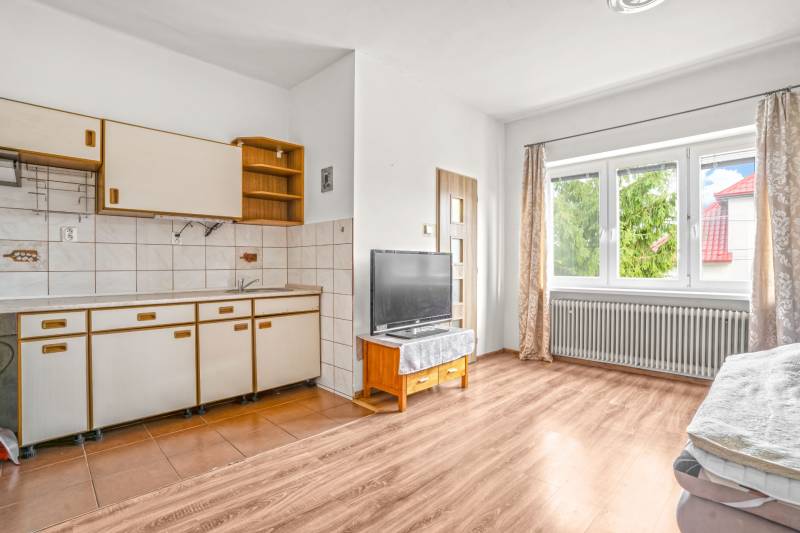 NA PREDAJ VÝNIMOČNÝ RODINNÝ DOM VO VEĽKOM MEDERI - Kuchyňa v rodinnom dome so starším nábytkom, televízorom a podlahou s dreveným dekorom.