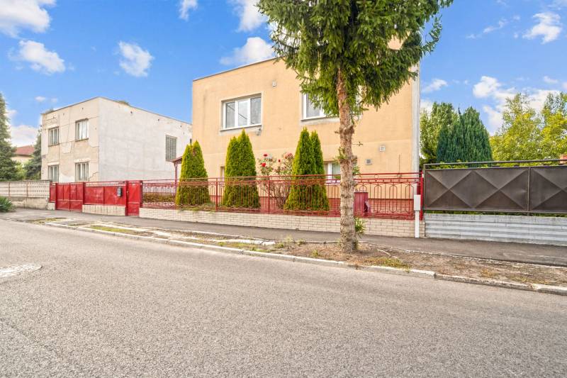 NA PREDAJ VÝNIMOČNÝ RODINNÝ DOM VO VEĽKOM MEDERI - Rodinný dom vo Veľkom Mederi s červeným plotom a stromami v predzáhradke.