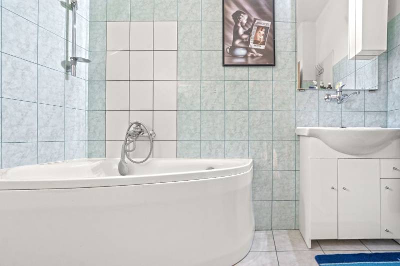 NA PREDAJ VÝNIMOČNÝ RODINNÝ DOM VO VEĽKOM MEDERI - Kúpeľňa v rodinnom dome s rohovou vaňou a umývadlom na svetlej dlažbe.