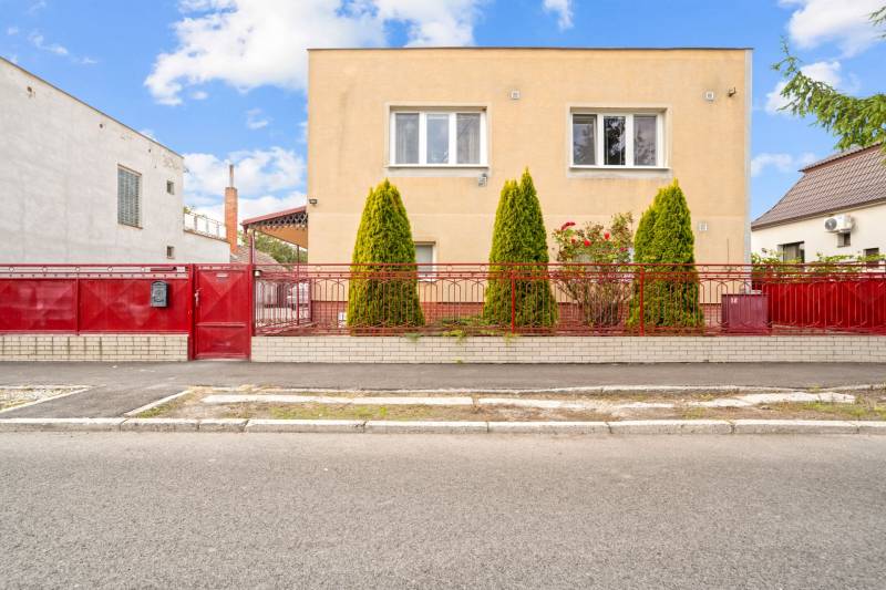 NA PREDAJ VÝNIMOČNÝ RODINNÝ DOM VO VEĽKOM MEDERI - Rodinný dom vo Veľkom Mederi so žltou fasádou, červeným plotom a zeleňou pred domom.