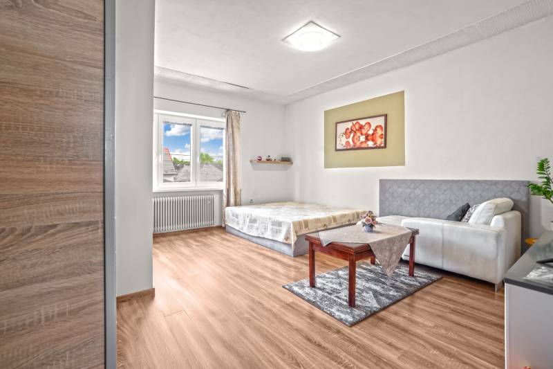 NA PREDAJ VÝNIMOČNÝ RODINNÝ DOM VO VEĽKOM MEDERI - Izba v rodinnom dome s posteľou, gaučom a podlahou s dreveným dekorom.