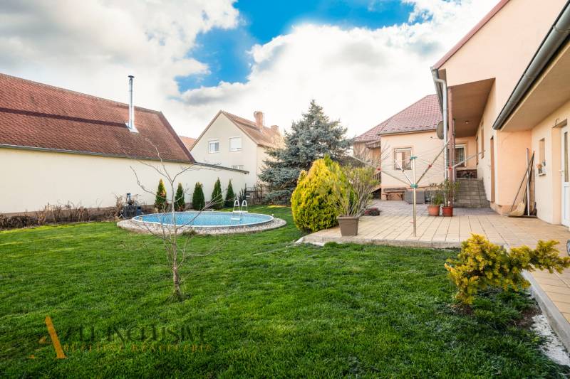 ZNÍŽENÁ CENA | NA PREDAJ DVOJGENERAČNÝ RODINNÝ DOM, AMADE KRAČANY - Rodinný dom na ulici Amade Kračany s bazénom a záhradou, obloha modrá, trávnik upravený.