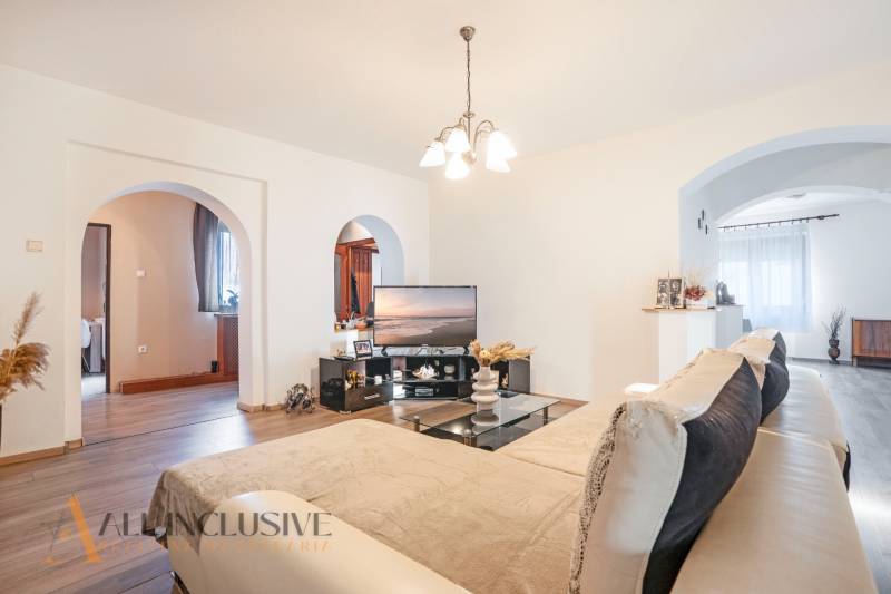 ZNÍŽENÁ CENA | NA PREDAJ DVOJGENERAČNÝ RODINNÝ DOM, AMADE KRAČANY - Obývačka na ulici Amade Kračany v rodinnom dome, pohodlný gauč, televízor, drevená podlaha.