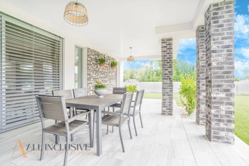 NA PREDAJ NADŠTANDARDNÁ 4-IZB. NOVOSTAVBA, DUN. KLÁTOV - Terasa rodinného domu v Dunajskom Klátove s jedálenským stolom a záhradnými rastlinami.