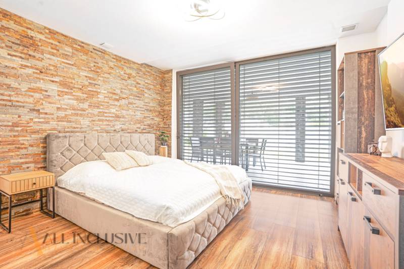 NA PREDAJ NADŠTANDARDNÁ 4-IZB. NOVOSTAVBA, DUN. KLÁTOV - Spálňa s kamennou stenou, pohodlnou posteľou a rozšíreným výhľadom cez okno v rodinnom dome.