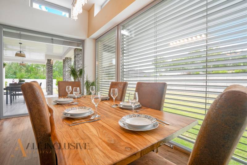 NA PREDAJ NADŠTANDARDNÁ 4-IZB. NOVOSTAVBA, DUN. KLÁTOV - Jedáleň v rodinnom dome s dreveným stolom, prestretým riadom a výhľadom na terasu.