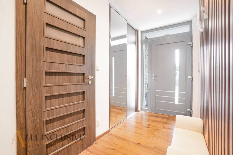 NA PREDAJ NADŠTANDARDNÁ 4-IZB. NOVOSTAVBA, DUN. KLÁTOV - Chodba v rodinnom dome s drevenou podlahou, zrkadlom a dverami s geometrickými prvkami.